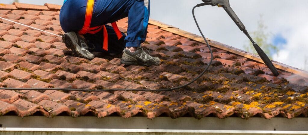 Man is washing the moss from the roof with a high pressure washer
